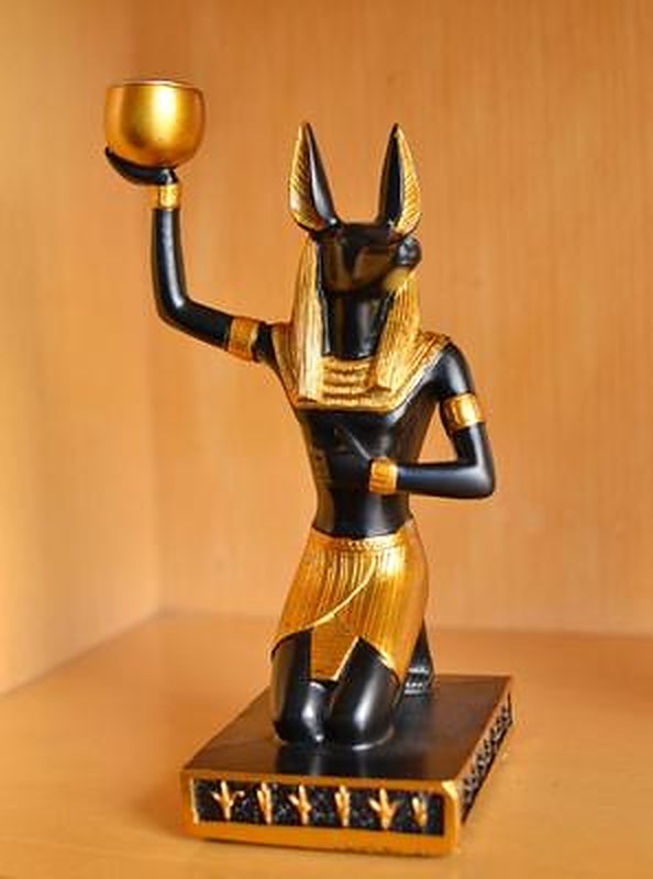 Statue Anubis vue de trois quarts — coupelle bougeoir dorée levée à bout de bras