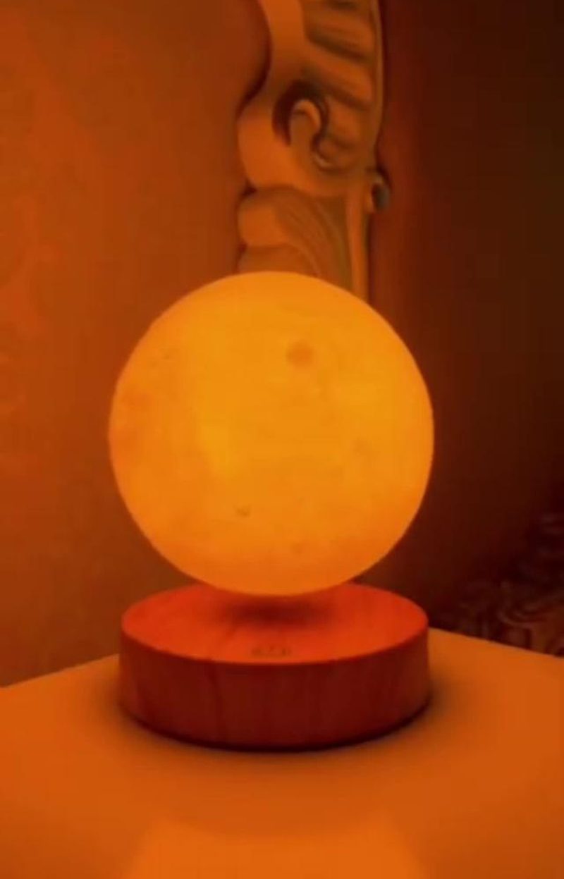 Lampe lune allumée en teinte chaude, posée sur une table près d'une tête de lit sculptée en bois, ambiance cocooning